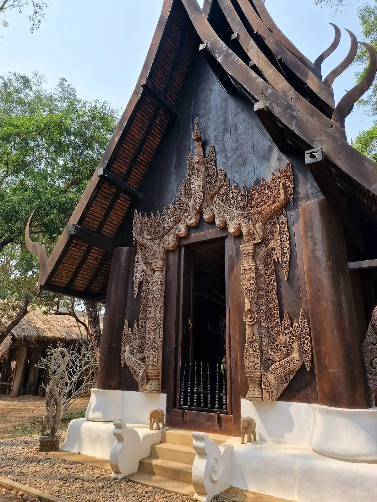 Ornate wooden building with intricate carvings and a steep roof, surrounded by trees.