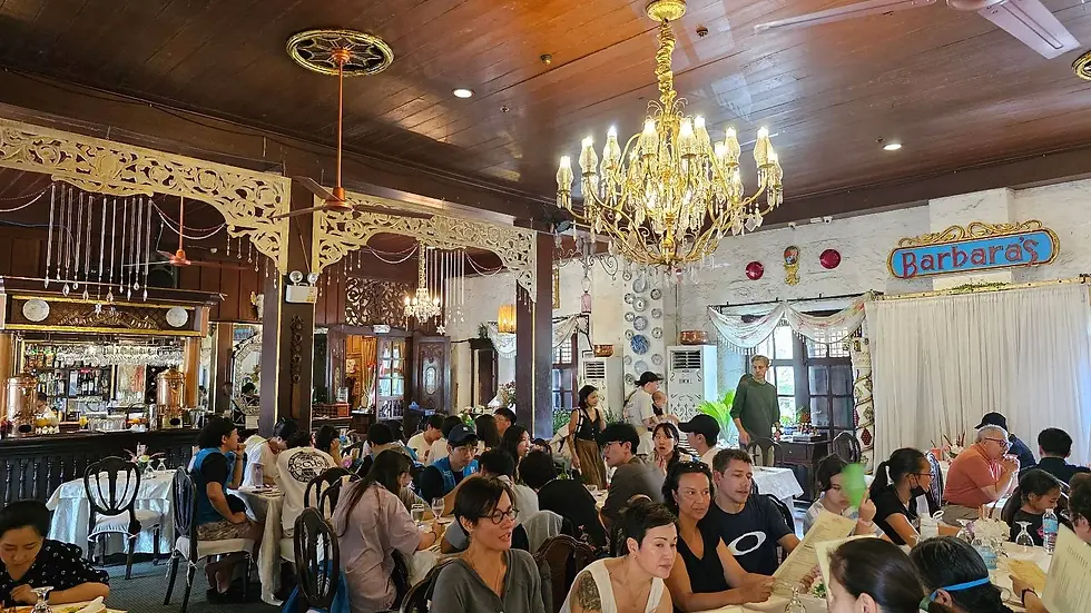 A crowded restaurant interior with wooden decor. People sit at tables eating and talking under a large chandelier.