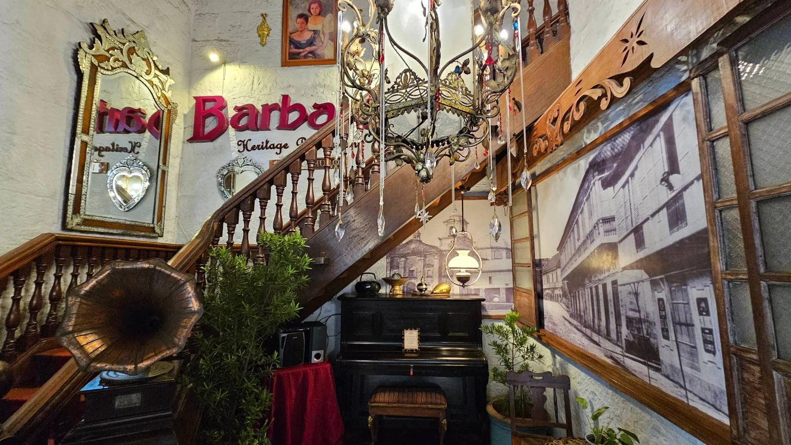 Vintage room with a grand staircase, chandelier, gramophone, piano, and framed photos. Text reads "Barba's Heritage." Cozy, nostalgic vibe.