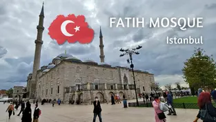 Fatih Mosque in Istanbul under cloudy sky, with visitors walking; white text and Turkish flag graphic overlay.
