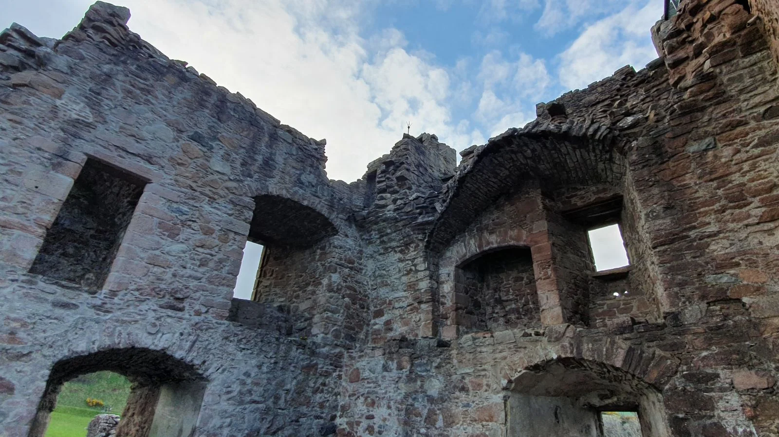 Interior ruins of Urquhart Castle in Scotland, showing stone walls, empty window openings, and partial arches against the sky.