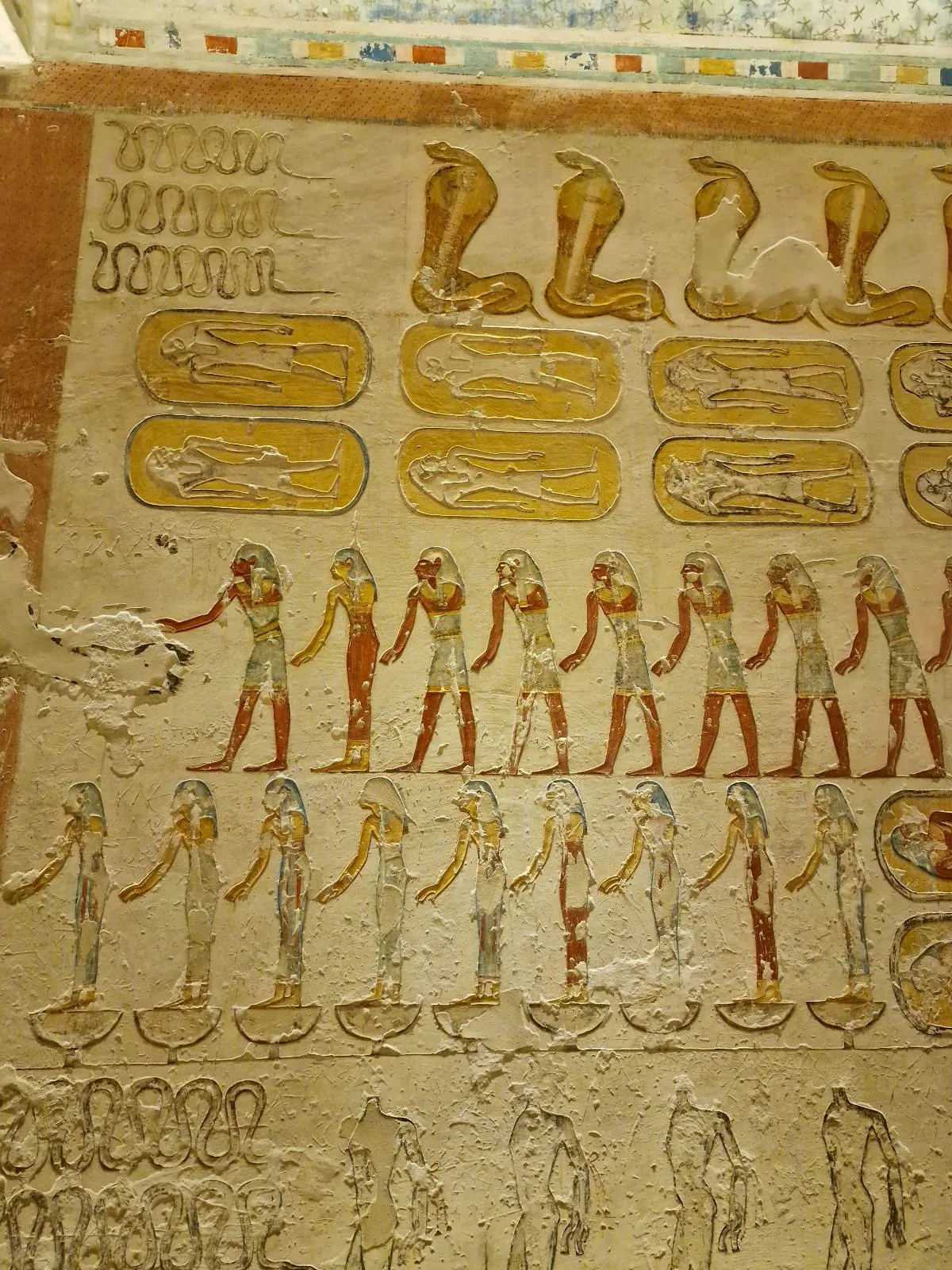 Ancient Egyptian wall art showing hieroglyphics and figures in traditional attire lined up in rows. The artwork is in shades of brown, yellow, red, and white.