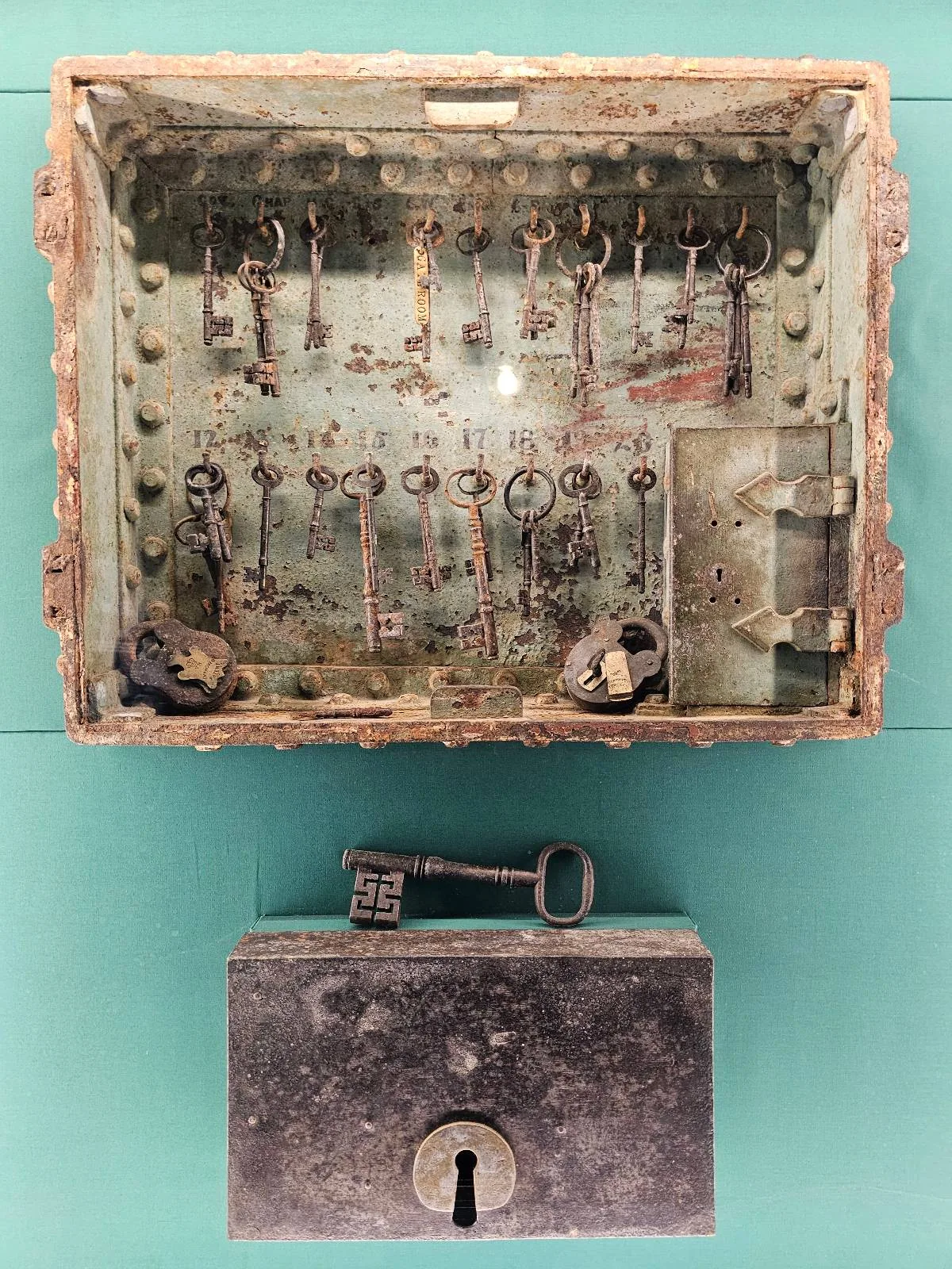 Vintage skeleton keys displayed in a worn shadowbox above a floral-patterned chest, mounted on a pale turquoise wall.