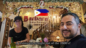 Two people in a vintage-style restaurant with ornate wooden decor. A sign reads "Barbara's Heritage Restaurant." Text overlay says, "A restaurant straight out of the 1800s!.