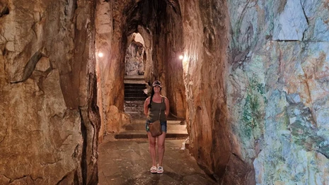 A woman standing in a stone corridor inside Marble Mountain, Da Nang, with carved rock walls and arched passages.