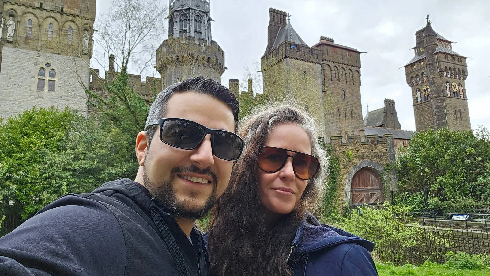 A couple wearing sunglasses posing for a selfie with a historic castle in the background.
