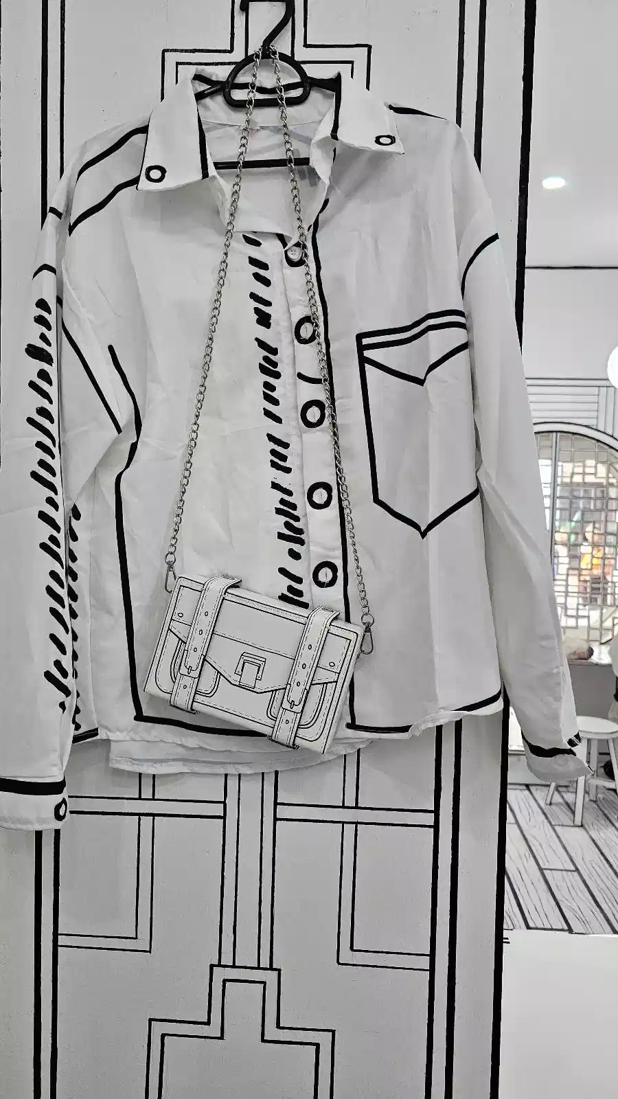 A jacket and bag hang against a wall, designed with bold, cartoon-like black outlines, creating a 2D illustrated effect. The jacket features prominent buttons and a pocket, while the bag has a visible strap and buckle.