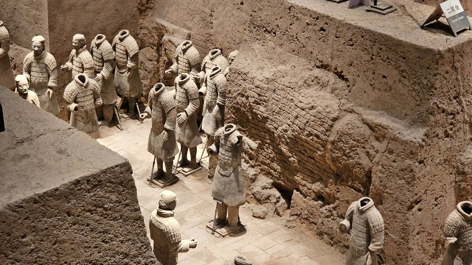 An excavated pit displays rows of headless terracotta warrior statues, standing in formation within ancient earthen walls, part of the famous Terracotta Army in Xi'an, China.