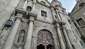 A close-up view of the ornate stone facade of San Agustin Church, highlighting the intricately carved wooden doors and classical columns of the UNESCO World Heritage site.
