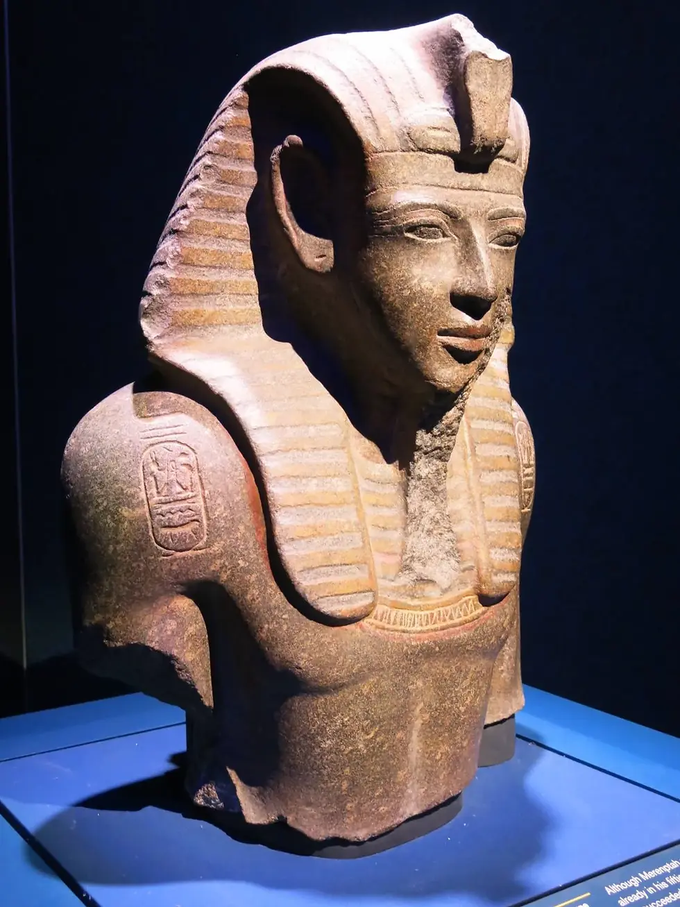 A weathered bust of an ancient Egyptian pharaoh wearing a nemes headdress, displayed on a blue stand against a dark background.