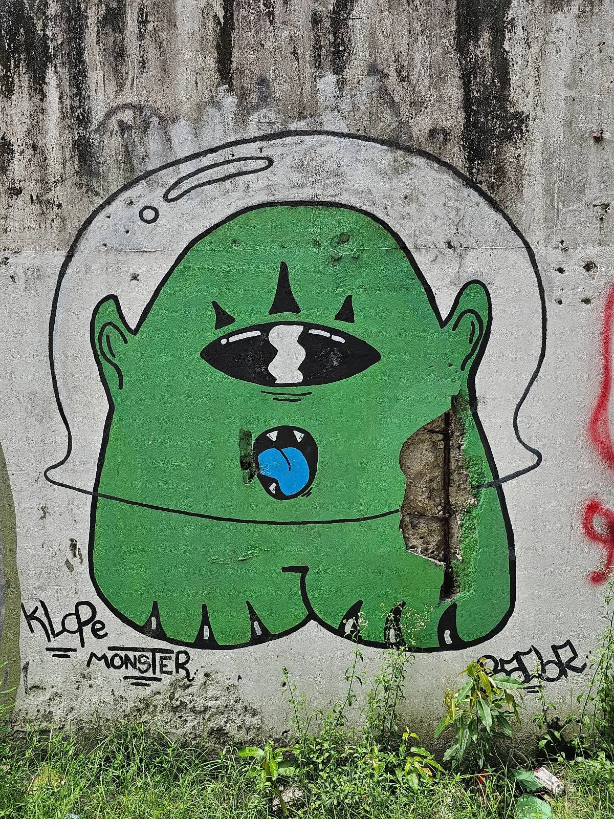 Graffiti of a green monster with one eye and a globe in its mouth on a concrete wall, signed by "klope monster".