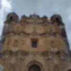 Ornate church facade with intricate carvings and statues, under a cloudy sky. Earthy tones and weathered details create a historic feel.