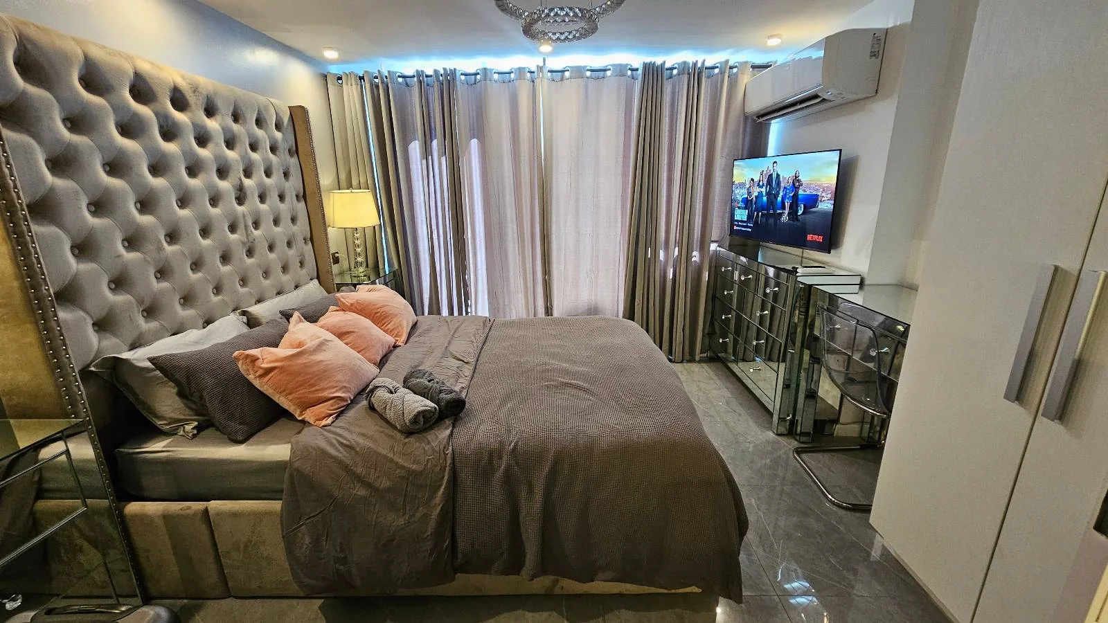 A bedroom with a bed, mirrored chest of drawers, a TV and a wardrobe.