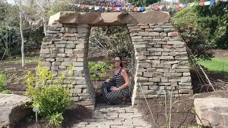 Jenn sitting beneath a stone arch in the Royal Botanic Garden Edinburgh during a visit to the gardens.