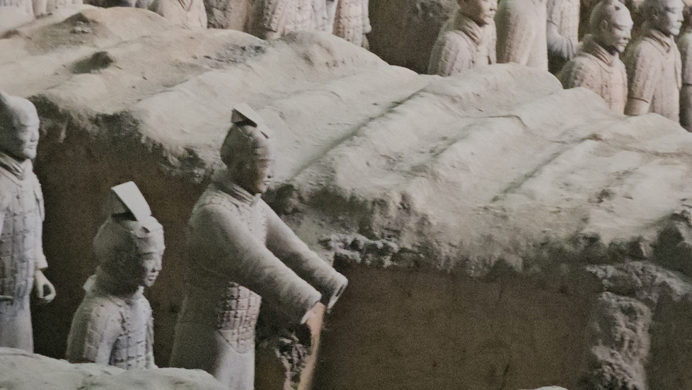 Terracotta statues of ancient Chinese warriors and horses stand in rows, partially buried in earth, as part of the famous Terracotta Army archaeological site in Xi’an, China.