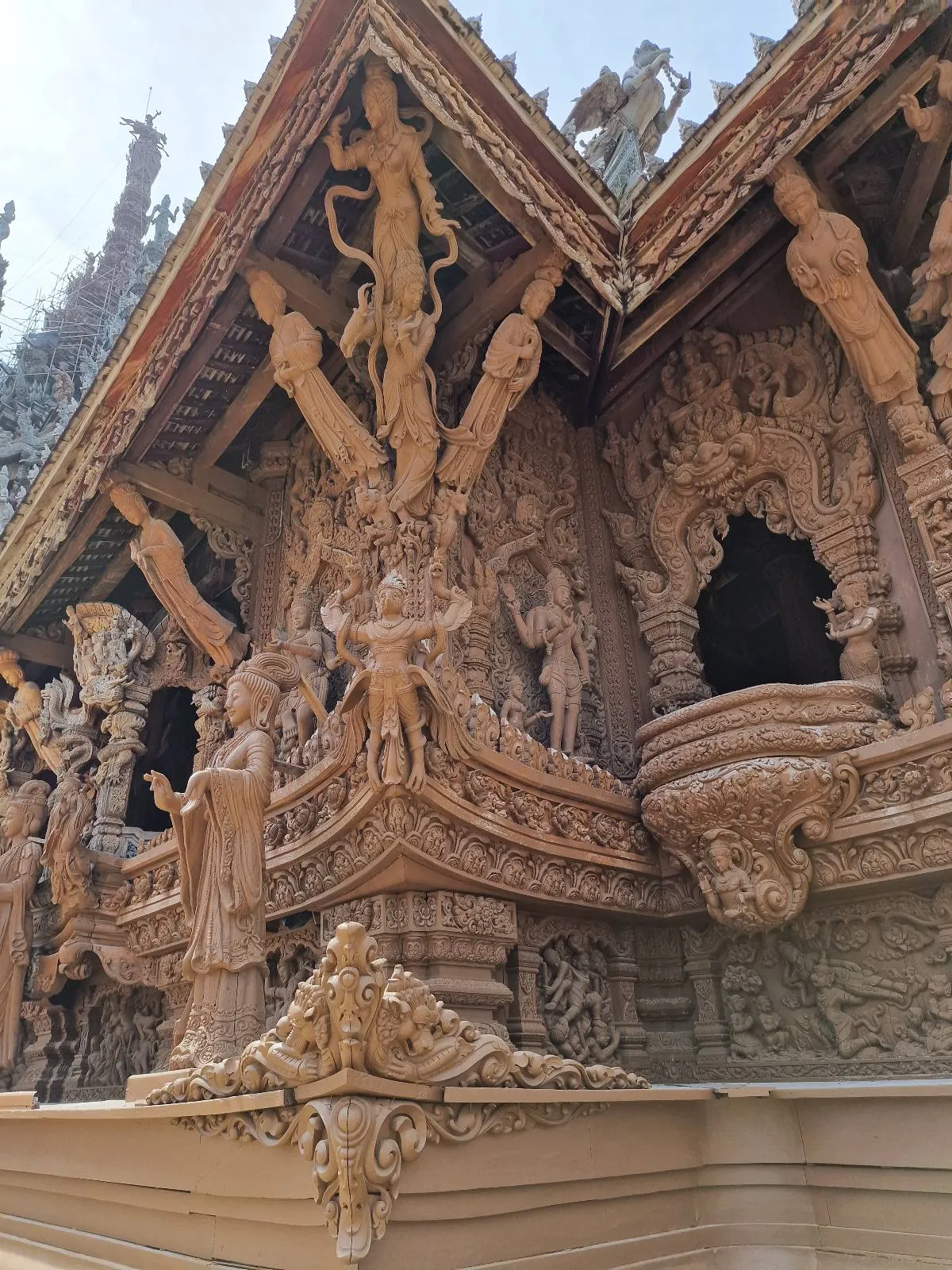 A detailed view of an intricately carved wooden temple facade with statues and ornate decorations, showcasing figures and patterns, set against a clear sky.