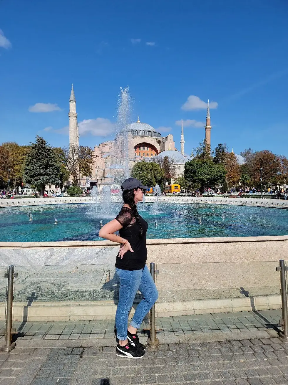 Person standing by a fountain with a historic mosque in the background under a clear blue sky.