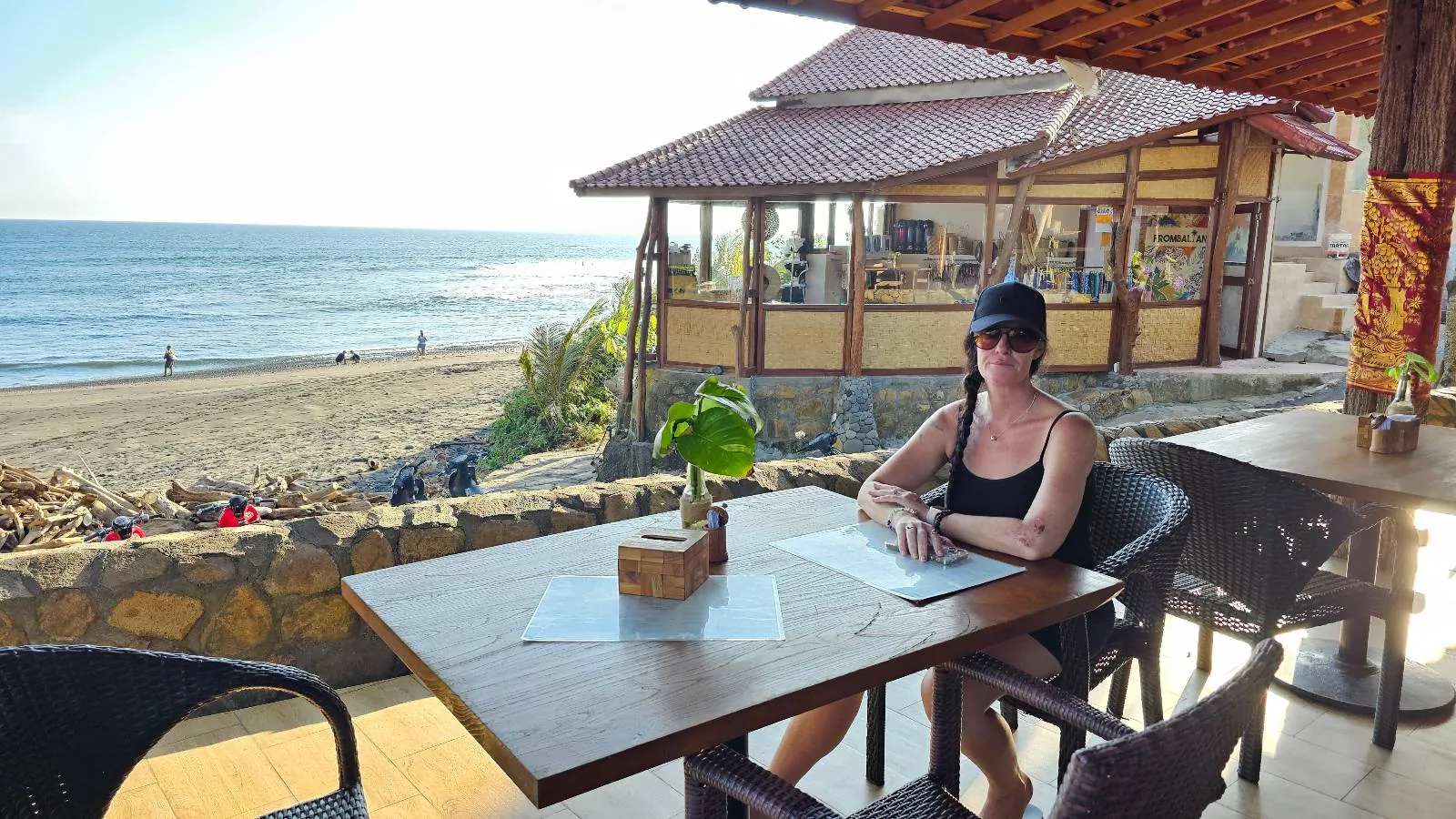 A square white plate on a wooden table holds grilled chicken wings arranged on a banana leaf, garnished with fresh parsley.