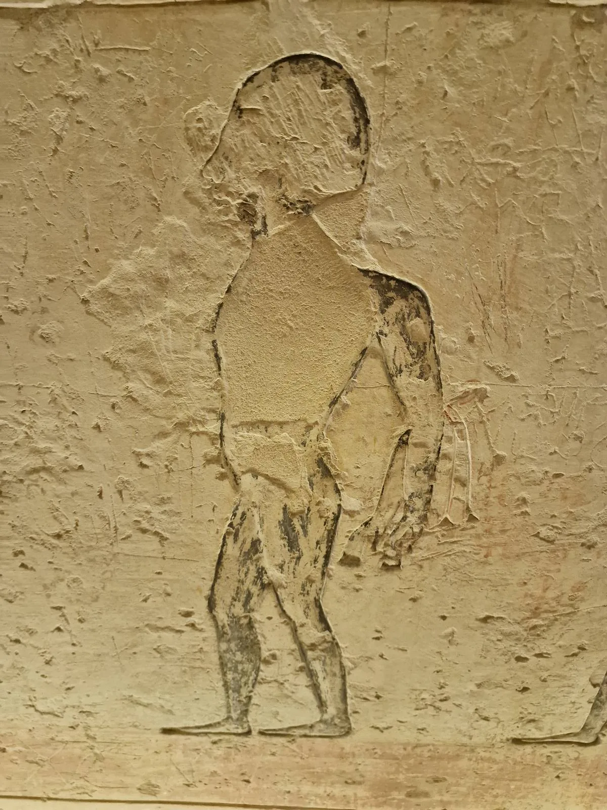 An ancient Egyptian wall carving depicts a figure in profile walking and carrying an object, with worn and faded details.