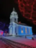 A church and tree adorned with colorful lights in a snowy setting at night, creating a festive and serene atmosphere.