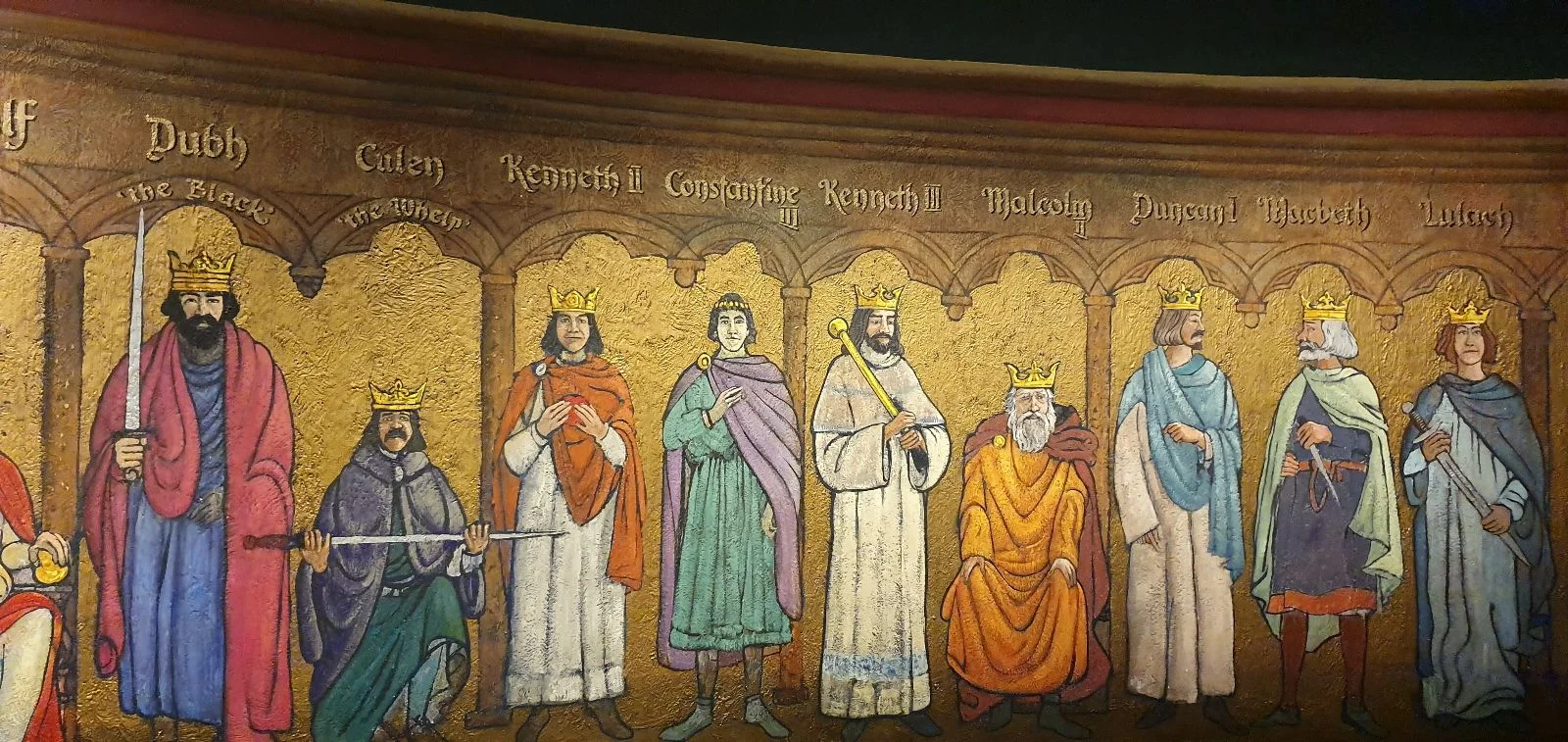 Medieval-style mural showing a line of historical figures in robes, each holding symbolic items, set against a decorative gold background.