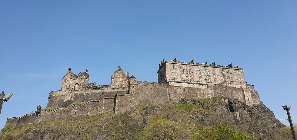 Stone castle on a rocky hill under a clear blue sky. The structure has multiple buildings with varying heights and styles. No text visible.