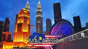 Night view of Kuala Lumpur skyline featuring lit-up buildings and Petronas Twin Towers; Malaysia flag graphics and the word "MALAYSIA" overlaid in bold text at the center bottom.