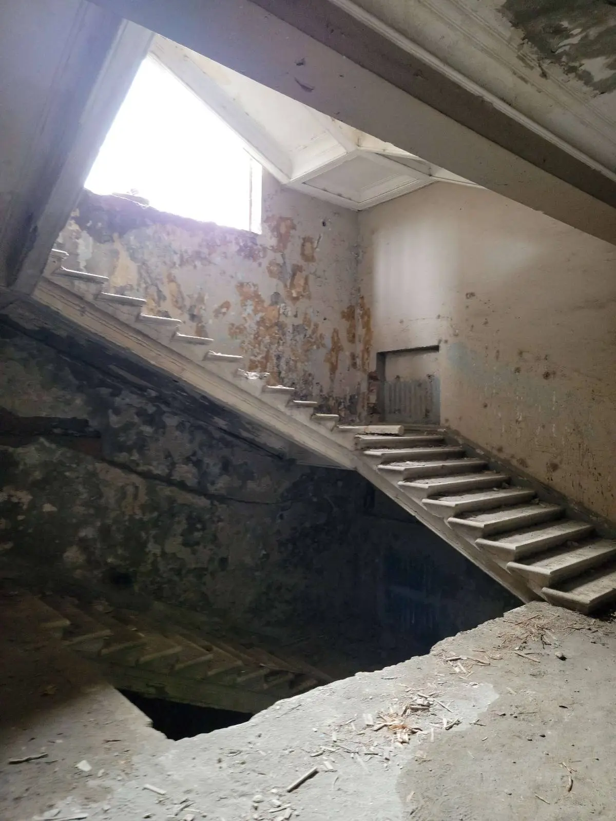 Dilapidated interior stairway in an abandoned building with peeling paint and debris.