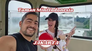 Two people smiling and pointing at a sign inside a cable car with "Taman mini Indonesia Indah, Jakarta" text overlay.