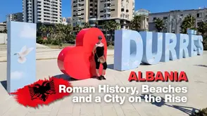 Person poses by large "DURRËS" letters in a cityscape, with bold text "ALBANIA" and "Roman History, Beaches and a City on the Rise."