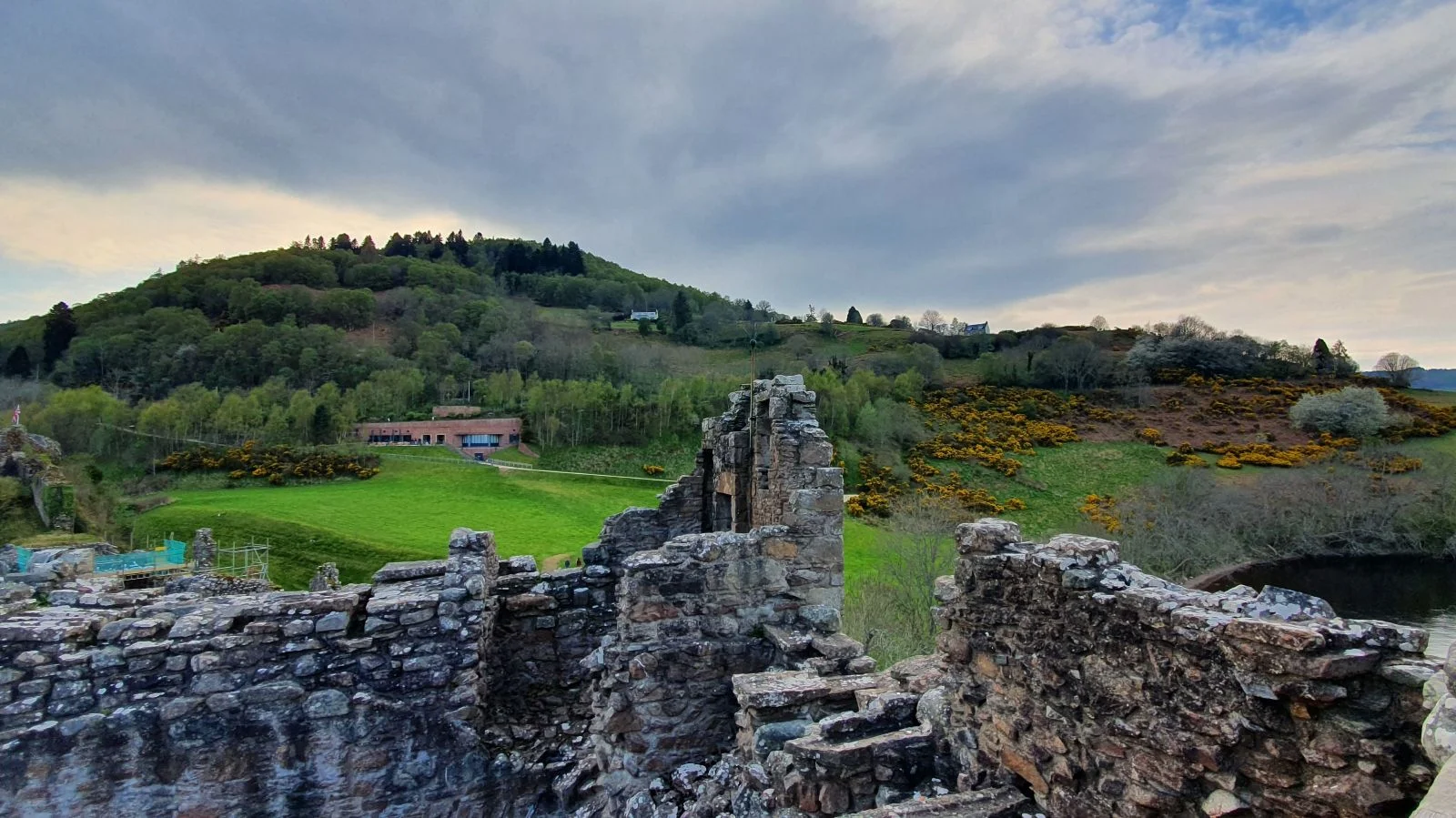 Urquhart Castle ruins with surrounding green hills and woodland in the Scottish Highlands.