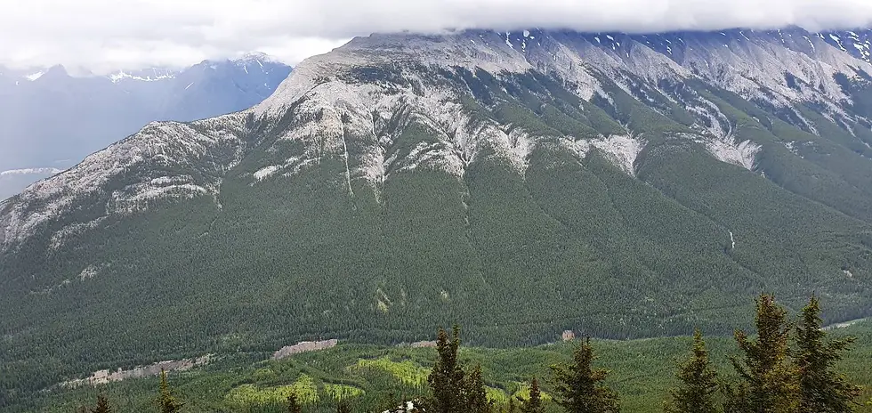 A vast mountain range covered with dense green forest under a cloudy sky.