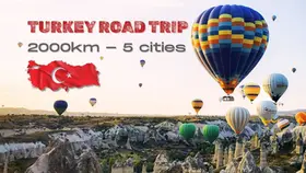 Hot air balloons in colorful patterns float over Cappadocia's rocky landscape. Text: Turkey Road Trip 2000km – 5 cities. Turkey flag.