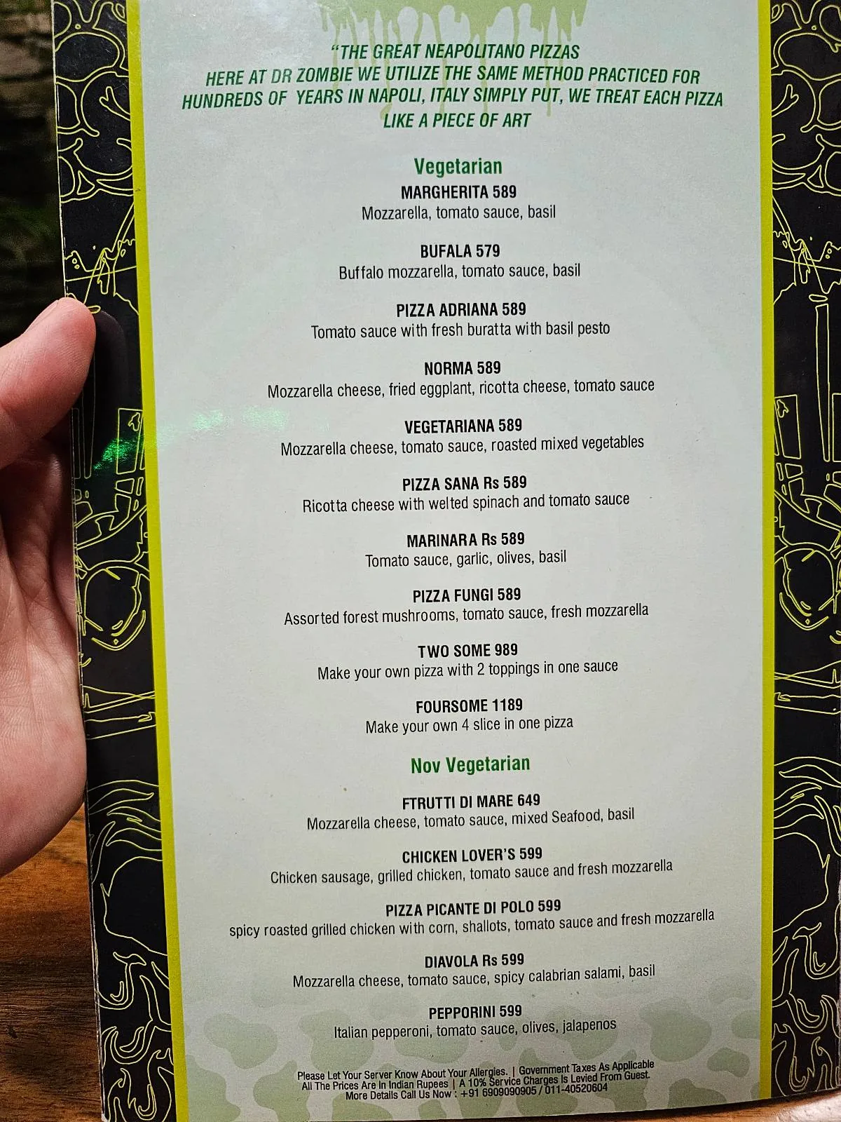 A hand holds a restaurant menu listing various vegetarian, vegan, and non-vegetarian curries, along with their ingredients and prices, on a green and white background.