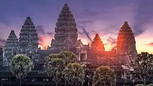 Angkor Wat temple complex silhouetted at sunrise with palm trees and dramatic sky in Siem Reap.