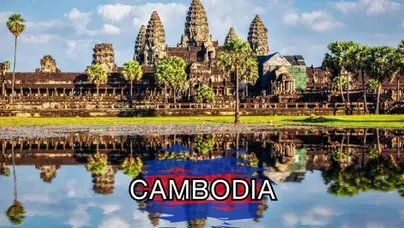Ancient stone temple of Angkor Wat in Cambodia with palm trees, reflected in a pond, under a blue sky; "CAMBODIA" in bold text over a red and blue paint-like background at the bottom.