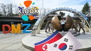 Person posing with bronze statues near split globe sculpture at DMZ with "Klook" logo. South and North Korean flags in foreground.