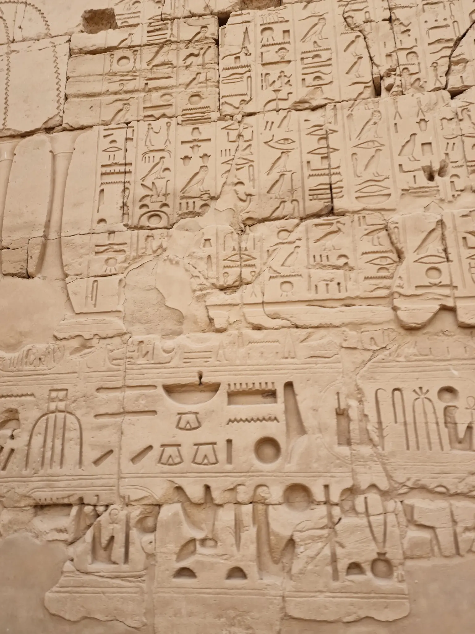 Ancient Egyptian hieroglyphs carved into a stone wall, depicting various symbols and figures. The carvings are weathered but still visible.