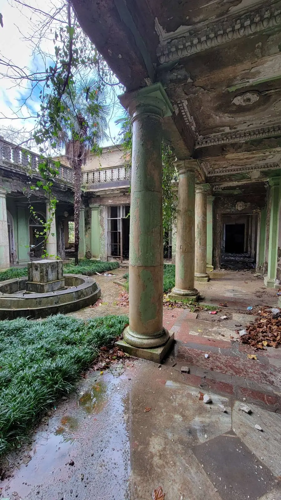 Decaying courtyard of an abandoned building with overgrown plants and deteriorating columns.