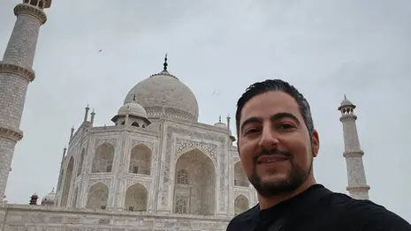 Man standing in front of the Taj Mahal in Agra with the monument fully visible behind him.