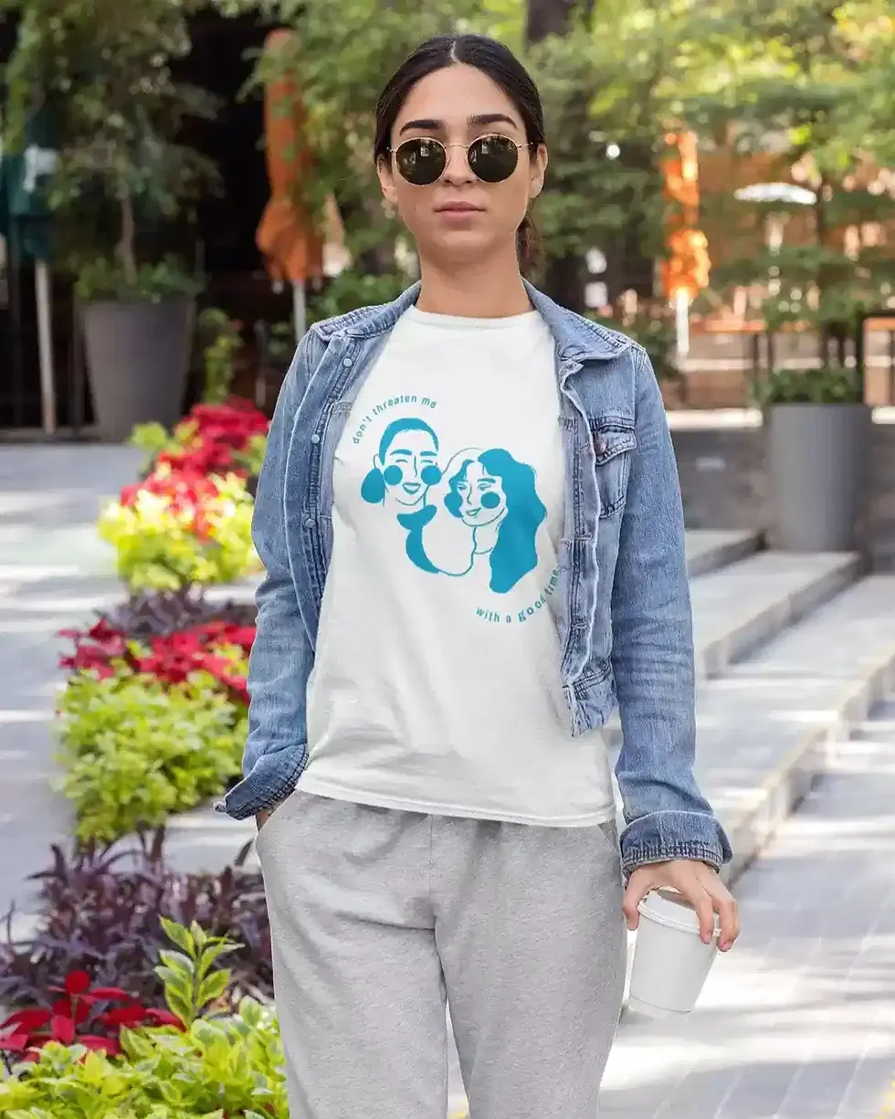 A person wearing sunglasses and a denim jacket walks outdoors, sporting a white T-shirt with a blue graphic design.