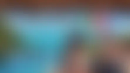 Two people in sunglasses smile by a pool with an ocean view. Palms and a thatched roof overhead. Text: "Isla Mujeres" with a heart.