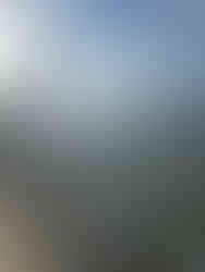 A pier with white pointed railings and decorative lanterns extends over calm water under a partly cloudy sky, with distant mountains visible in the background.