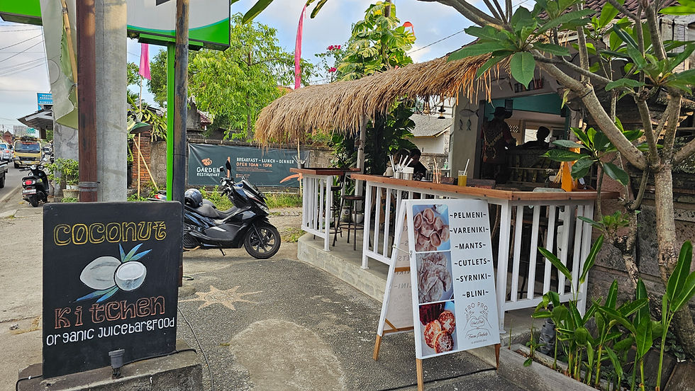Coconut Kitchen café with a thatched roof; sign reads "organic juice bar & food." Motorbike and plants outside on a sunny day.