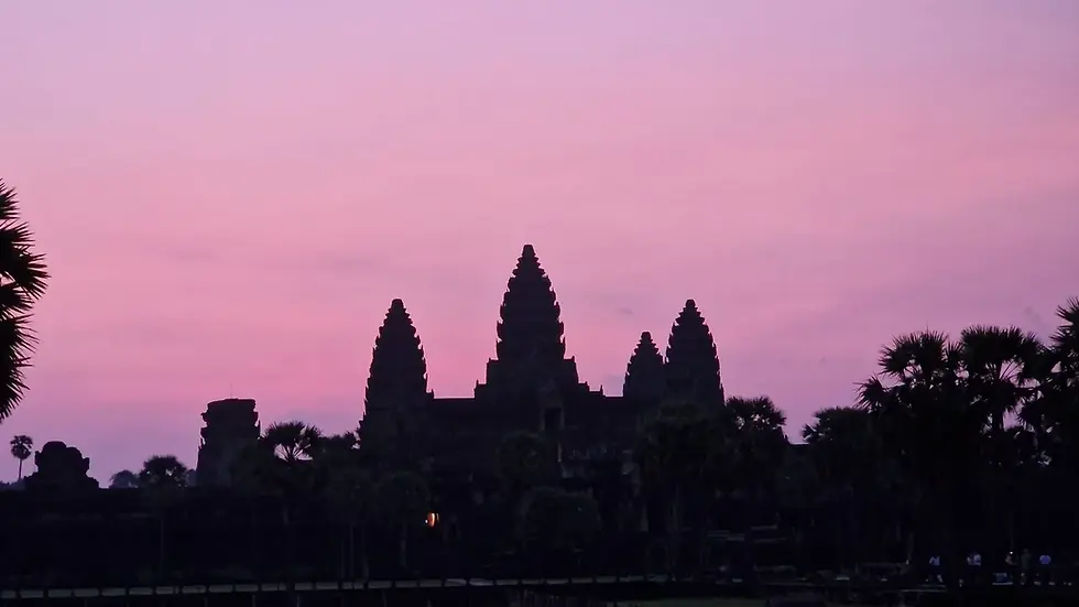 Silhouette of Angkor Wat against a pink-purple sunset, with palm trees in the foreground creating a peaceful, serene mood.
