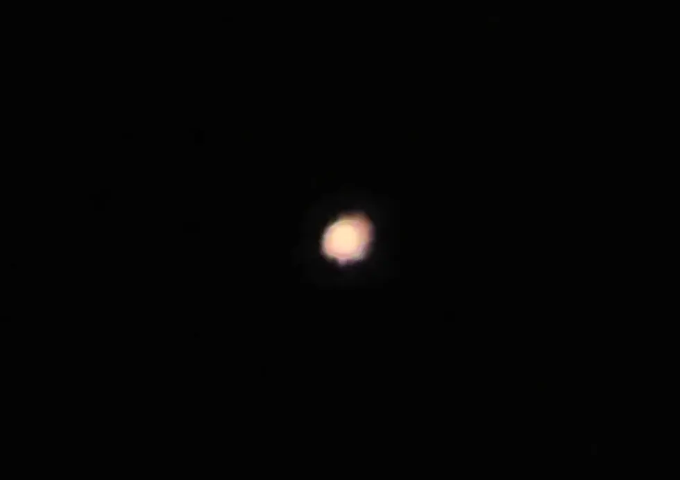 A bright, blurry orange light glows against a dark background, resembling a star or planet in the night sky.