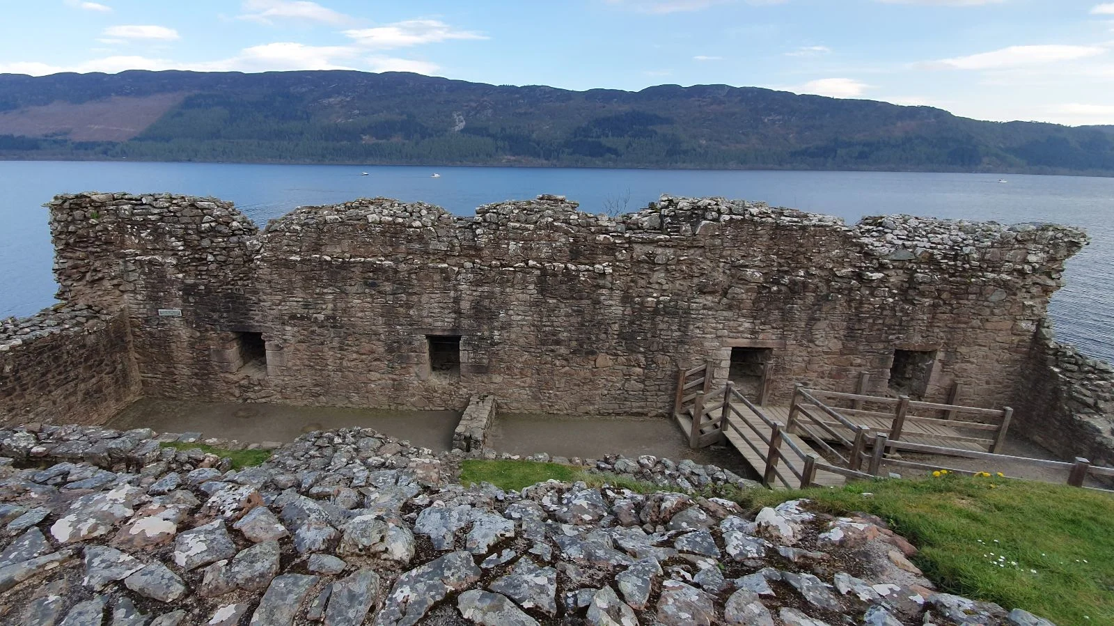 Stone walls of Urquhart Castle ruins overlooking Loch Ness, with visible doorways and steps along the structure.