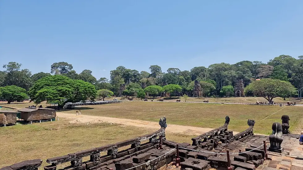 Ancient stone structures and statues in a grassy field with lush trees under a clear blue sky, creating a serene and historic atmosphere.