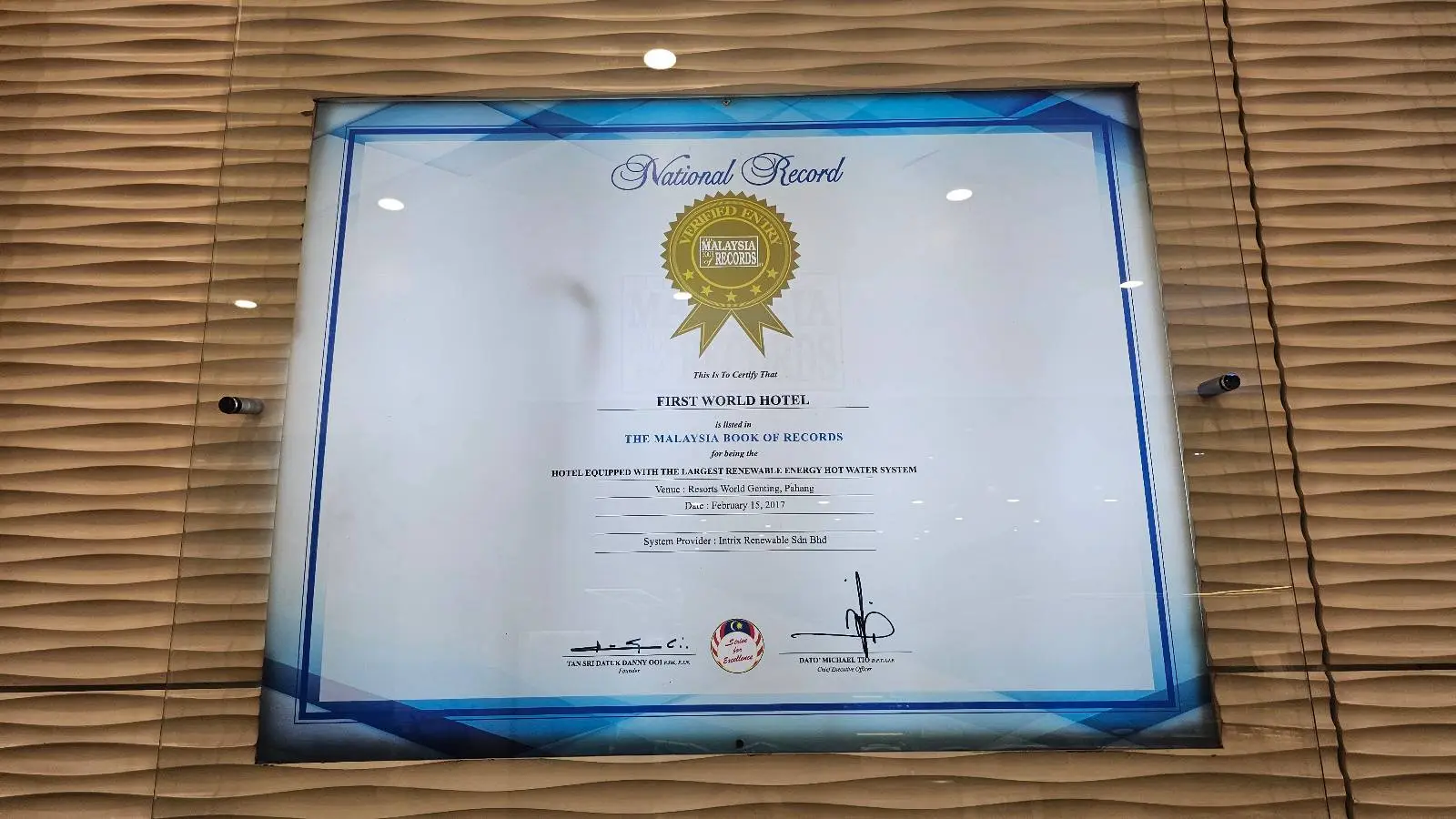 A framed award certificate with a gold seal displayed on a wall with a textured beige pattern. The text on the certificate is not fully legible in the image.