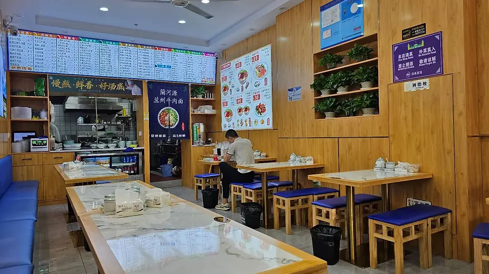 Man dining alone in a wooden interior restaurant with blue seats. Menu boards and plant decor in the background, creating a cozy ambiance.